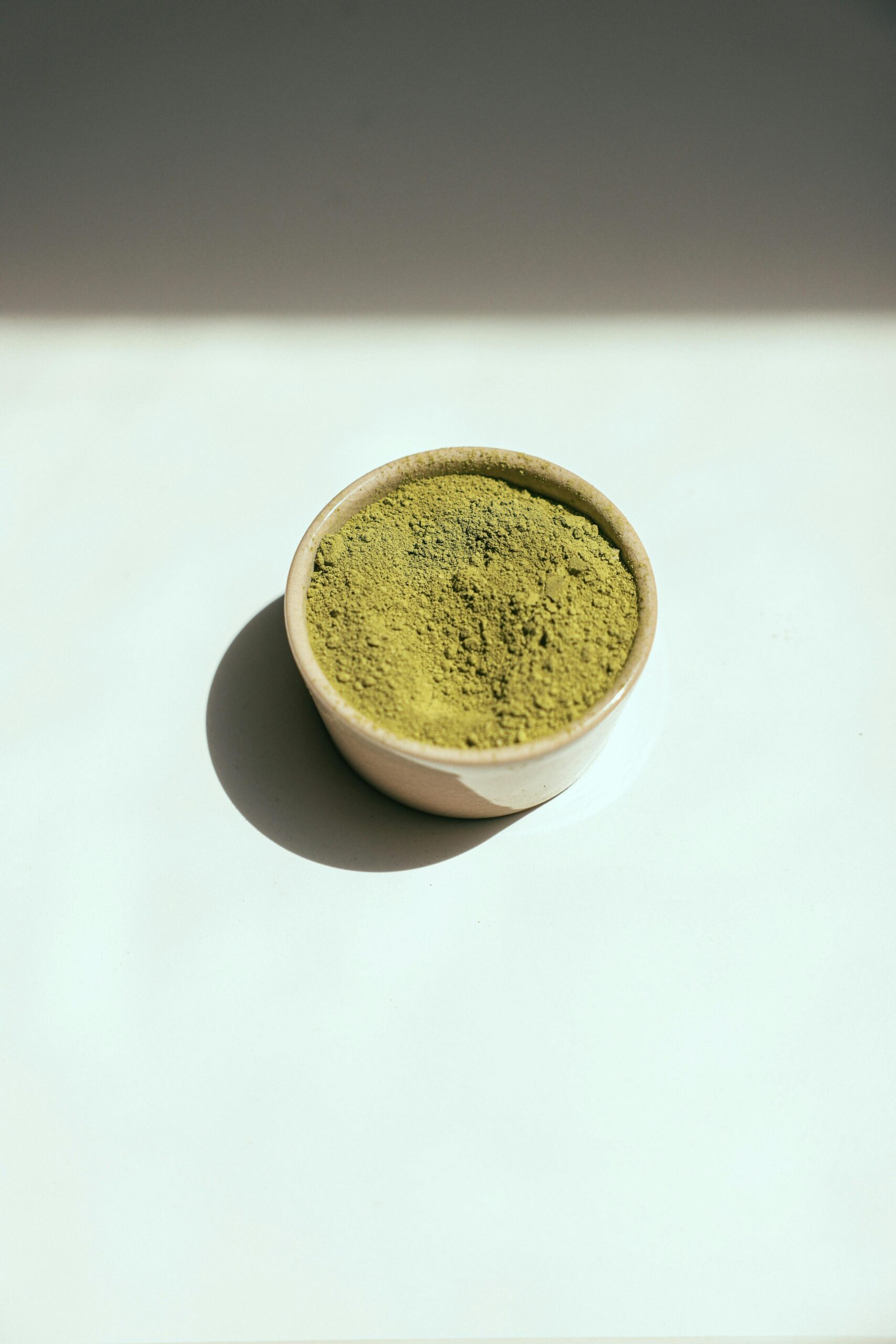 A minimalist ceramic bowl filled with vibrant green matcha powder on a white background.